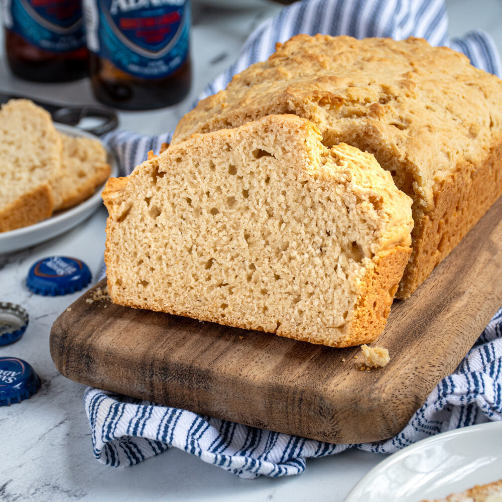 A slice of beer bread on a cutting board propped up against a loaf of easy beer bread.