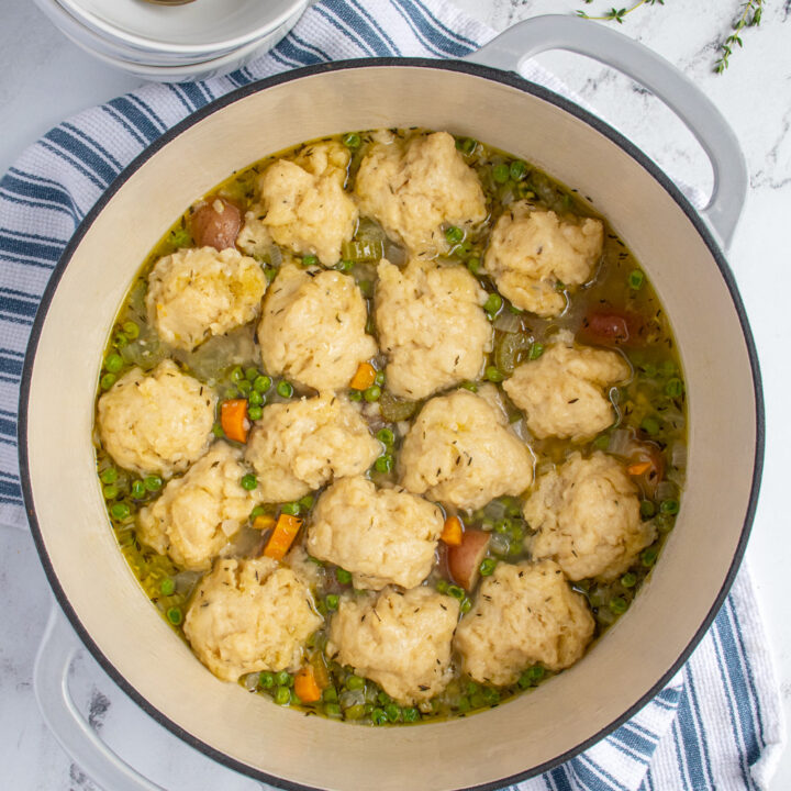 Overhead view of a dutch oven filled with veggie dumpling soup with carrots, celery, peas, and potatoes topped with dumplings.