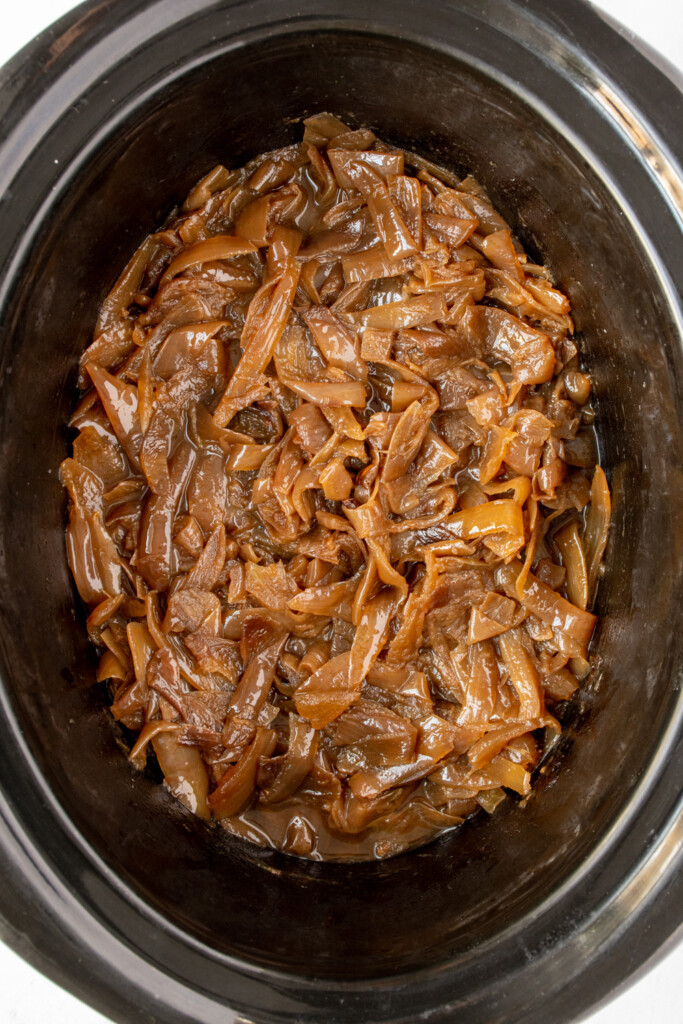 Slow cooker caramelized Onions in a black crockpot, the onions are a beautiful golden brown color.