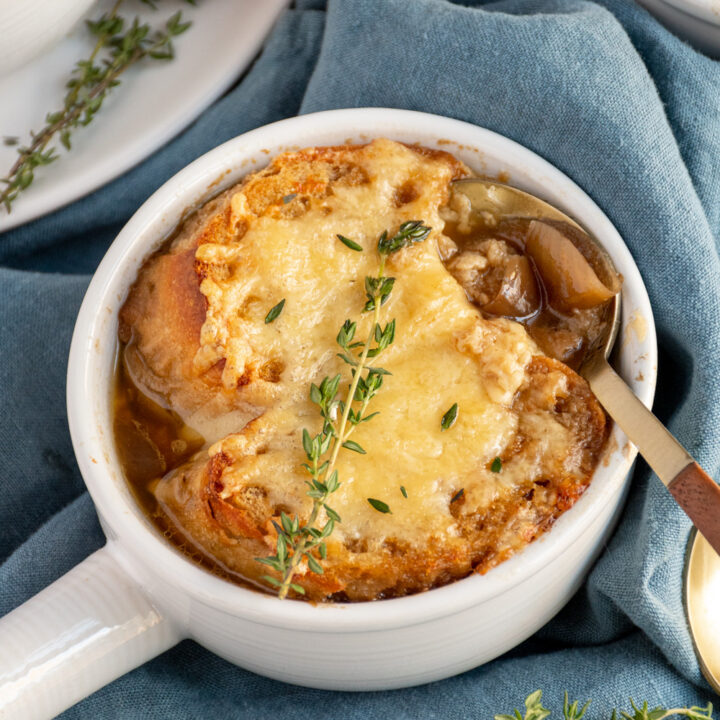 A spoon in a white bowl of French onion soup topped with baguette and melted cheese.