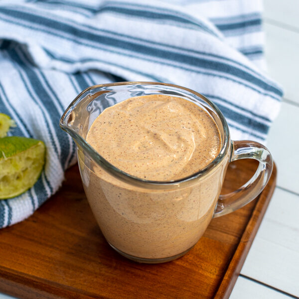 Serving glass with handle filled to the top with healthy southwest sauce sitting next to a kitchen towel and spoon.