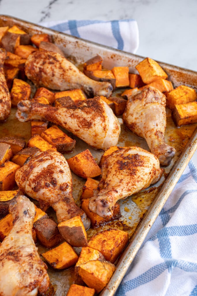 Photo of part of a sheet pan that is full of baked chicken legs and sweet potato chunks.