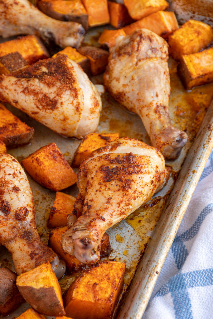 Close up of a chicken leg on a sheet pan surrounded by sweet potatoes.