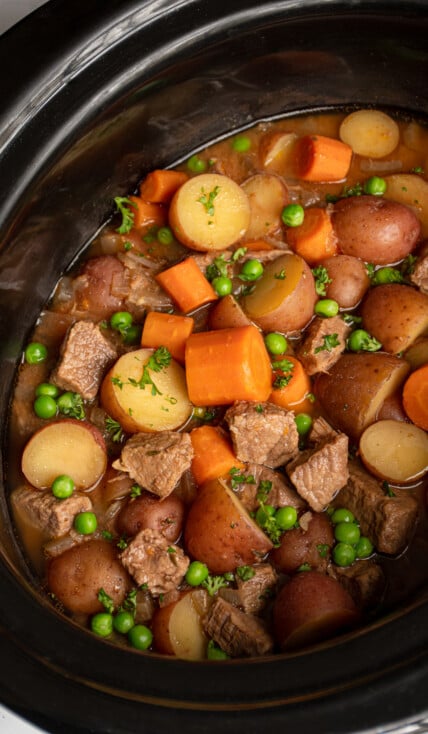 Crockpot full of beef stew filled with carrots, potatoes, chuck roast, and peas.