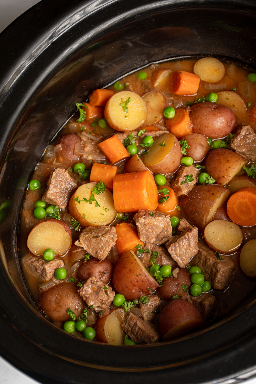 Crockpot full of beef stew filled with carrots, potatoes, chuck roast, and peas.