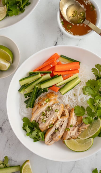 Overhead view of a large white bowl filled with vermicelli noodles and topped with lemongrass chicken, vegetables, and nuoc cham.