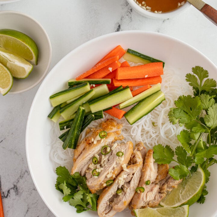 Overhead view of a large white bowl filled with vermicelli noodles and topped with lemongrass chicken, vegetables, and nuoc cham.