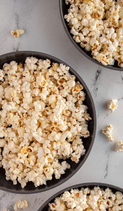 Three gray bowls with one in more center full of freshly popped popcorn that was made on the stovetop.