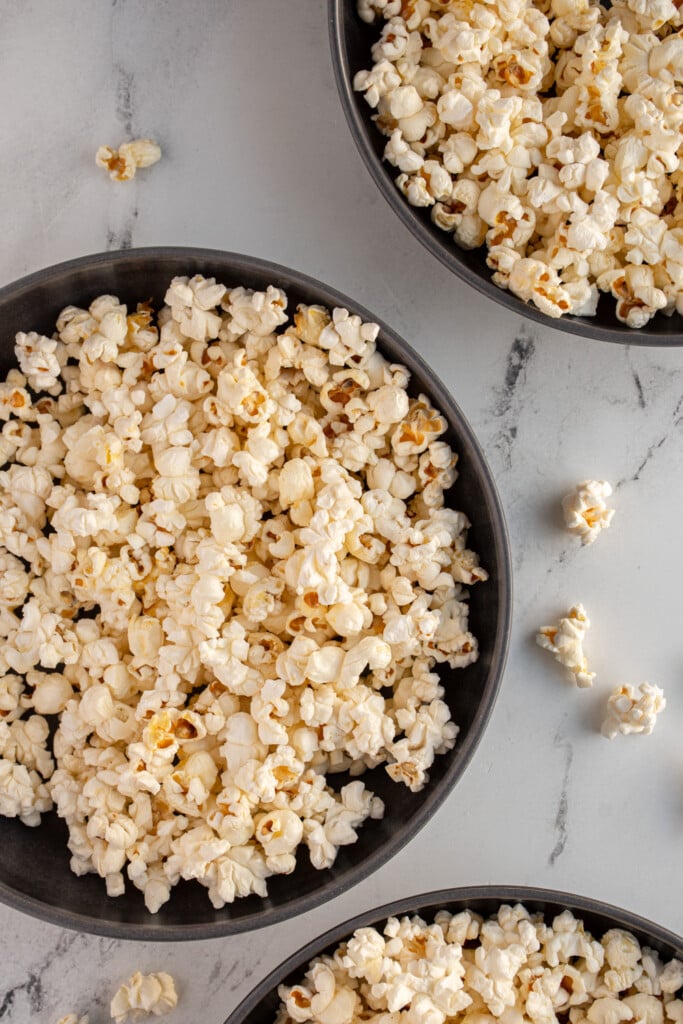 Three gray bowls with one in more center full of freshly popped popcorn that was made on the stovetop.