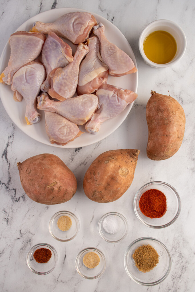 Ingredients needed to make sheet pan chicken legs and sweet potatoes laid out on a tabletop.