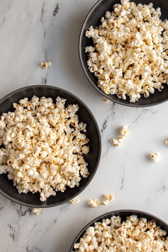 Overhead view of of three gray bowls for serving full of freshly popped stovetop popcorn.