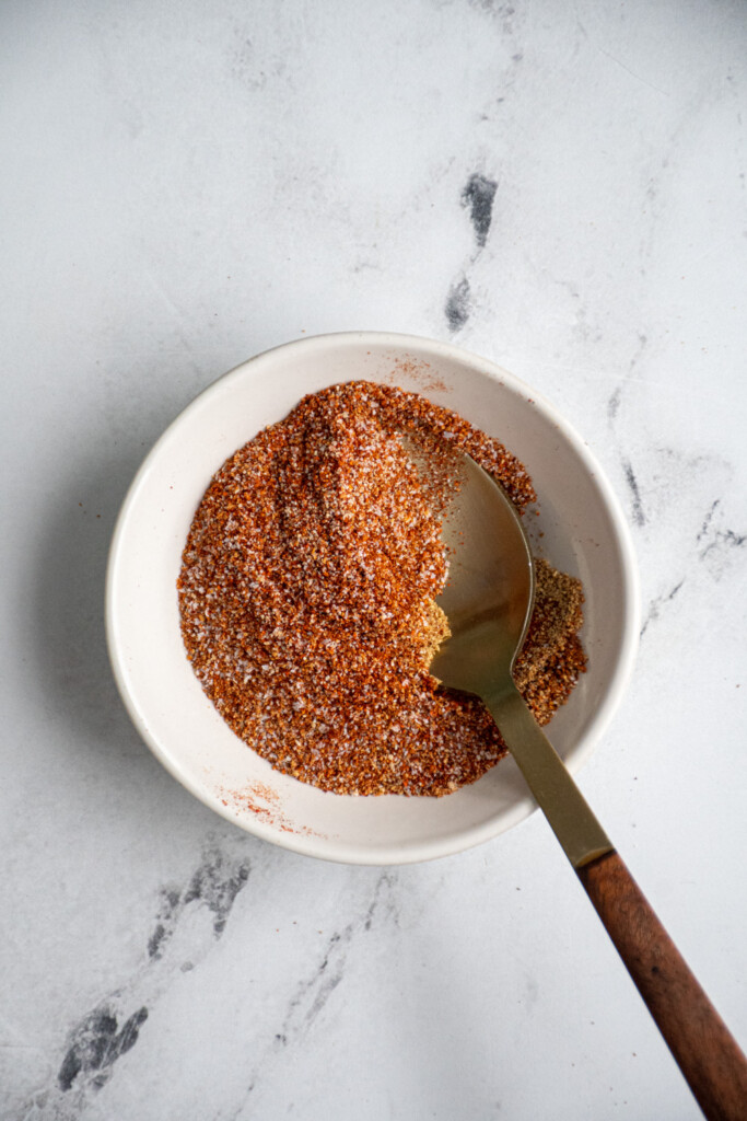 A small bowl with a spoon with the seasoning mixture for the chicken and sweet potatoes.