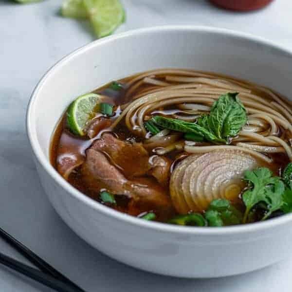 bowl of beef pho made in the slow cooker covered in green garnishes are ready to eat