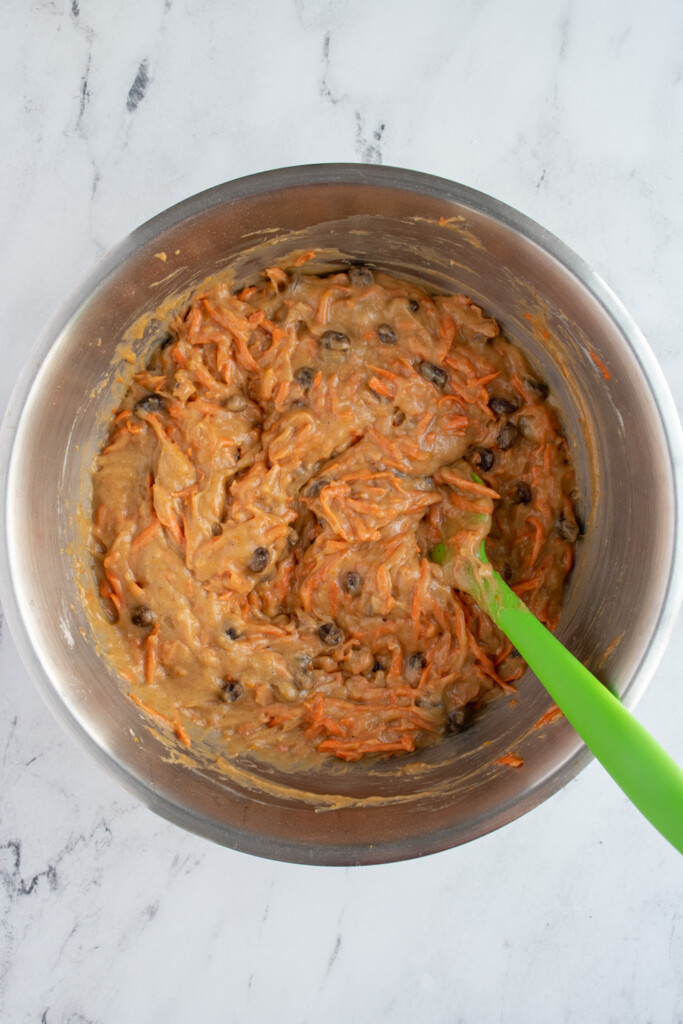 A stainless steel bowl filled with orange spiced carrot cake batter and a rubber spatula.