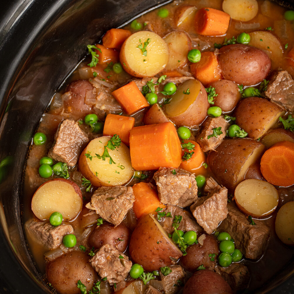 Crockpot full of beef stew filled with carrots, potatoes, chuck roast, and peas.