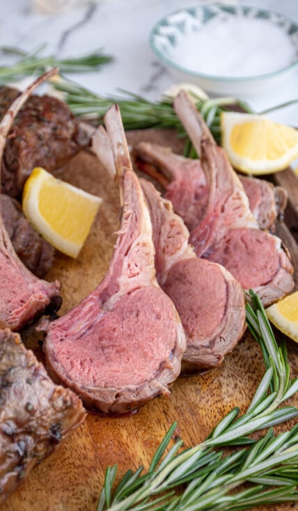 A few pieces of cut grilled rack of lamb on a wooden cutting board showing off the rosy interior color of the grilled lamb meat.