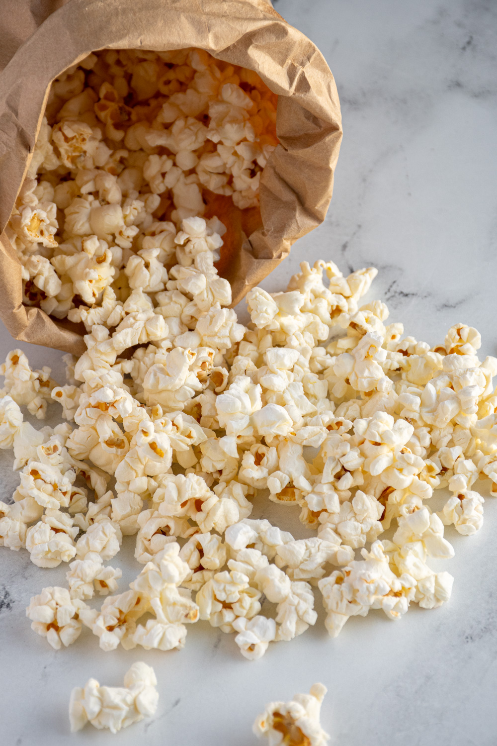 Popcorn cascading out of a brown paper bag after being cooked in the microwave.