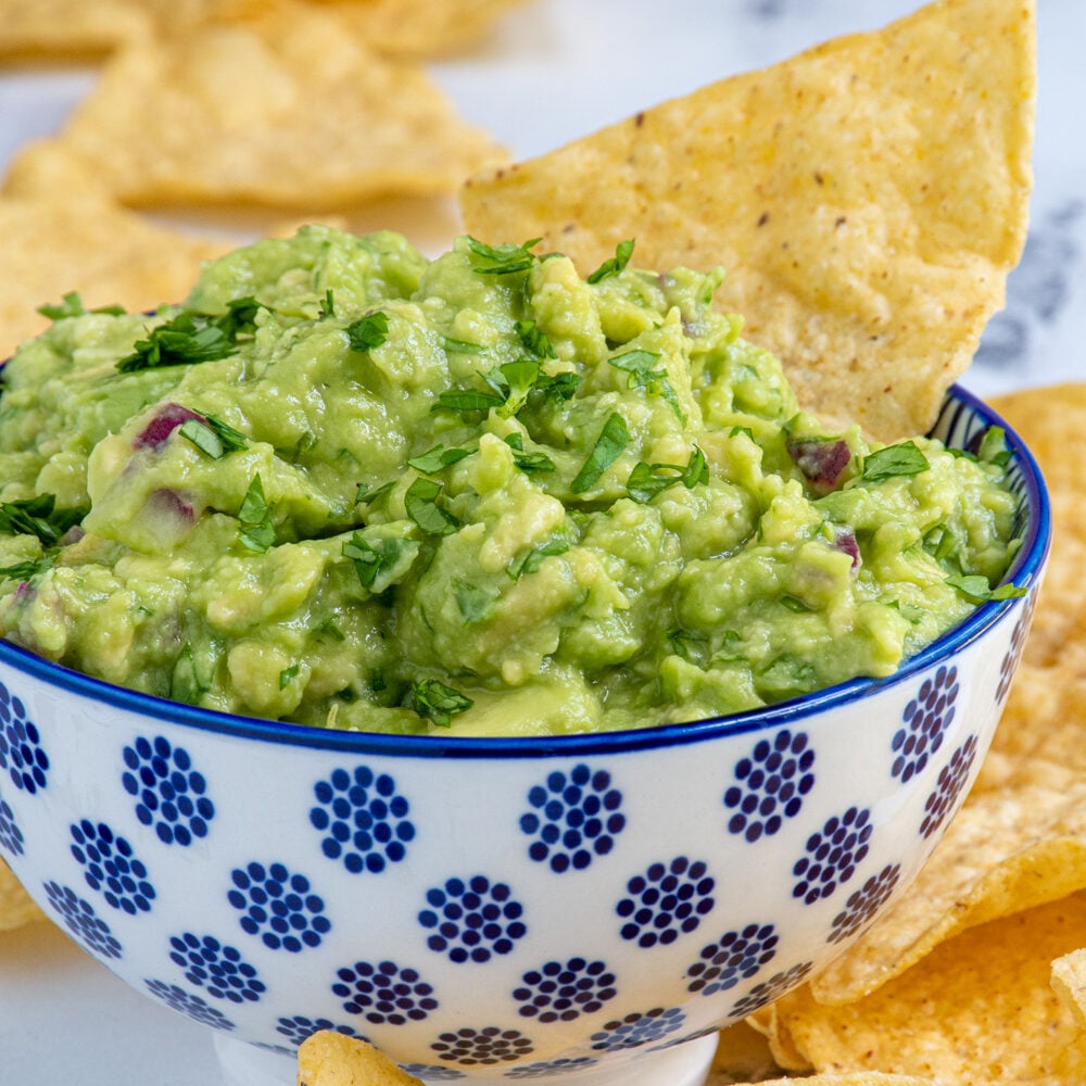 A blue and white bowl filled with simple guacamole and garnished with cilantro and with a tortilla chip.