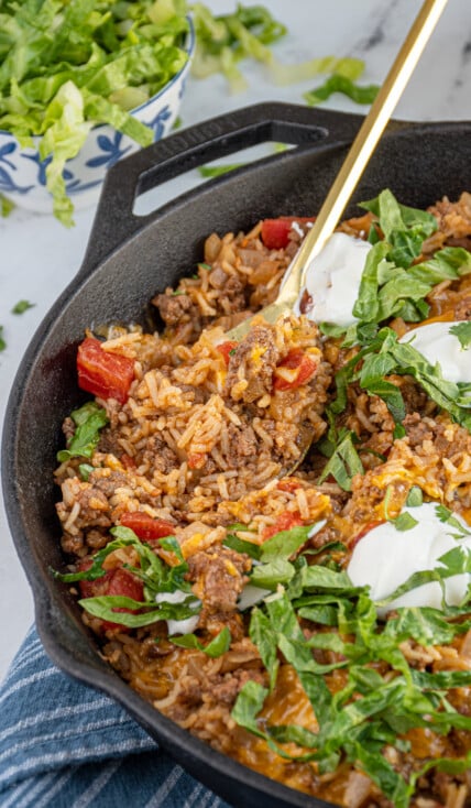 MexicanBeef Taco Rice Skillet in a cast iron pan with a spoon scooping to see the insides with ground beef and rice.