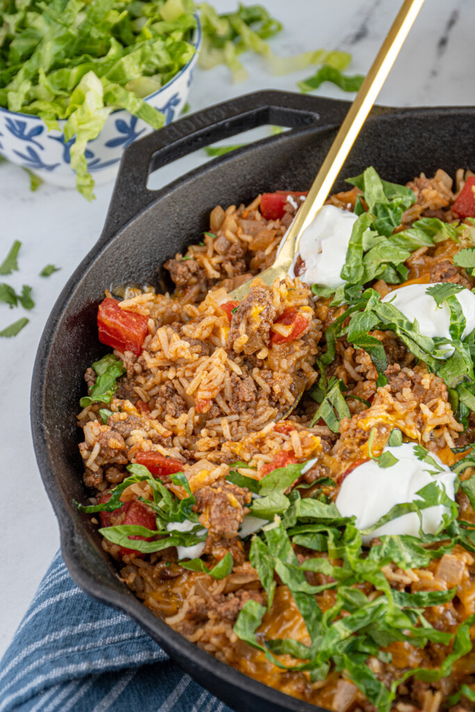 MexicanBeef Taco Rice Skillet in a cast iron pan with a spoon scooping to see the insides with ground beef and rice. 