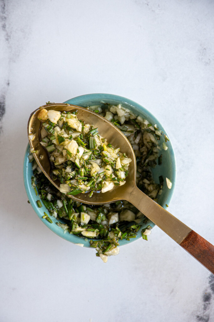 A small bowl with a spoon full of the olive oil, garlic, rosemary mixture for the grilled lamb.