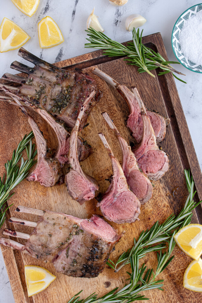 Overhead view of a wooden cutting board with a bunch of rack of lamb cut part into ribs for serving.