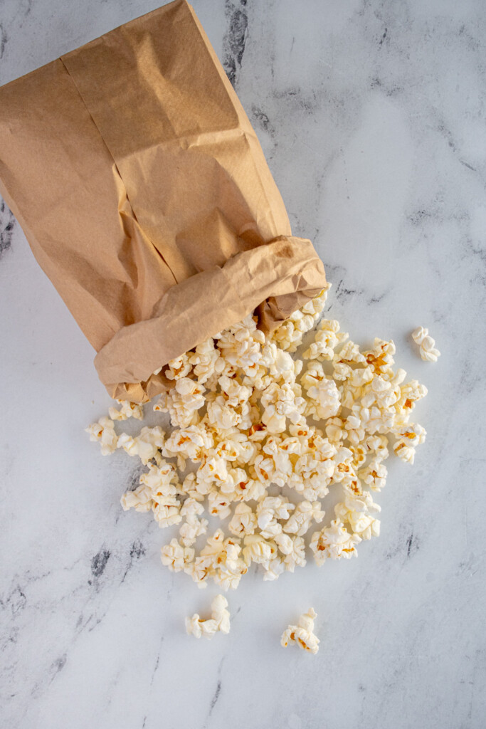 Overhead view of a brown paper bag opened up with freshly made popcorn coming out.