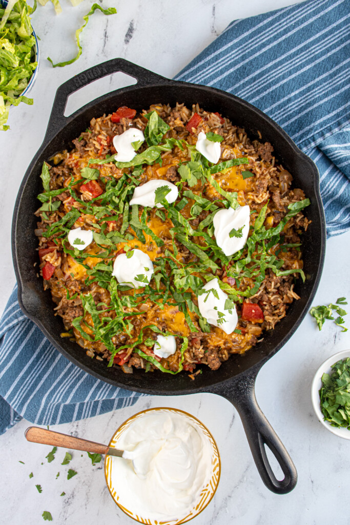 Overhead of taco rice skillet in a cast iron with ground beef, rice, tomatoes, cheese, lettuce, and sour cream.