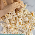 Pinterest pin with text overlay "Paper Bag Microwave Popcorn", image of a brown bag rolled up and popcorn tumbling out onto a tabletop.