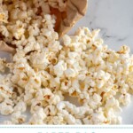 Pinterest pin with text overlay "Paper Bag Microwave Popcorn", image of a brown bag rolled up and popcorn tumbling out onto a tabletop.
