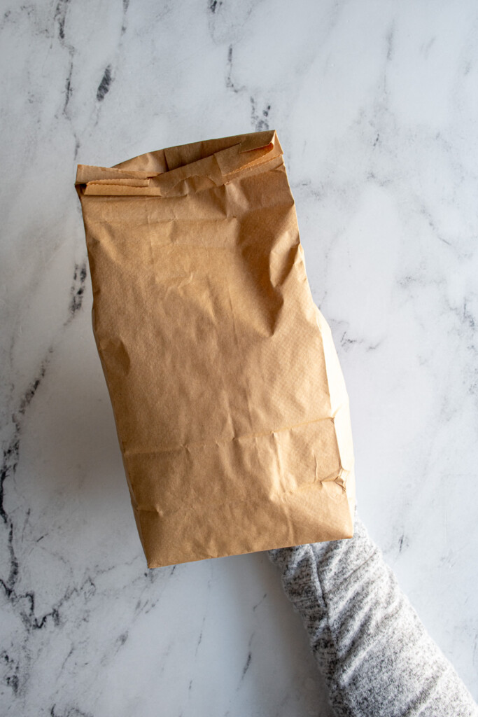 A brown paper bag filled with freshly popped popcorn from the microwave.