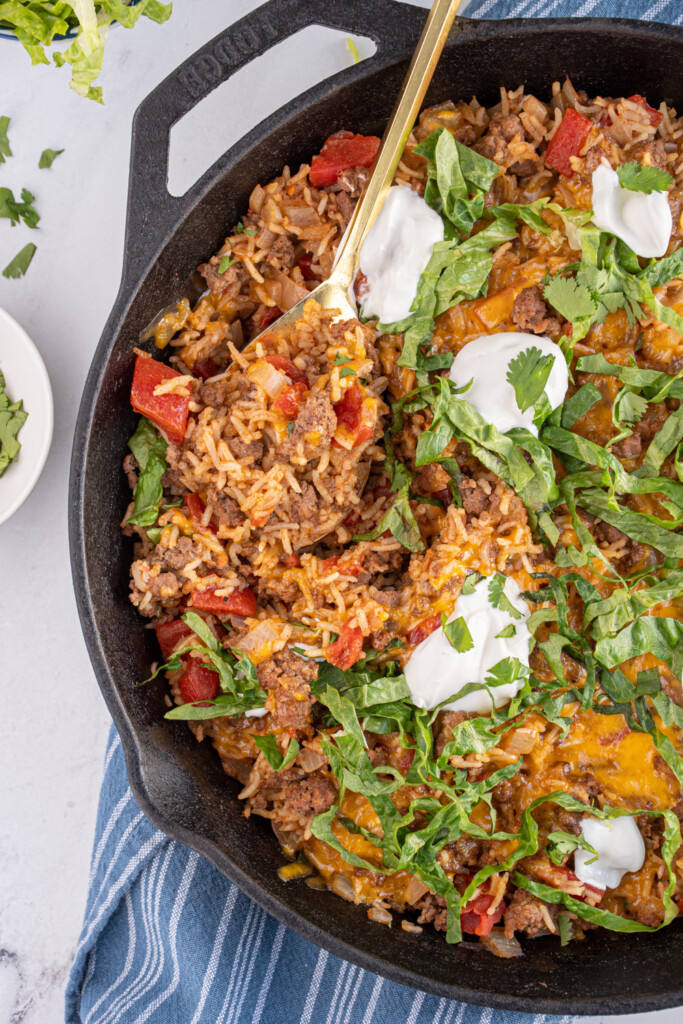 Overhead view of a spoon taking a scoop out of taco rice skillet showing the ground beef and rice.