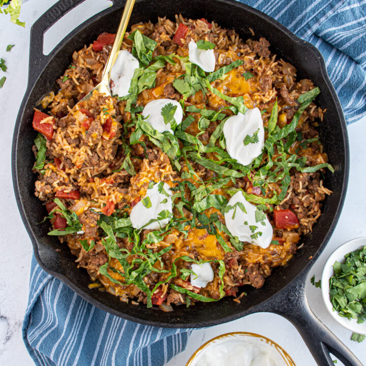 Taco rice fillet with Mexican beef, diced tomatoes, and rice toppediwht lettuce and sour cream with a serving spoon taking a scoop out.