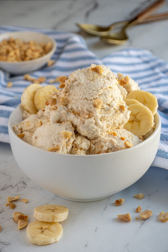 White bowl of banana cottage cheese ice cream garnished with peanut pieces.