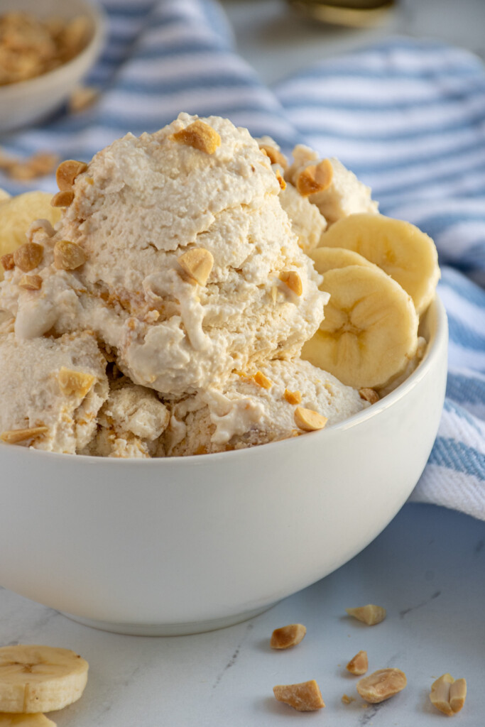 Close up of cottage cheese ice cream in a bowl garnished with peanuts and banana slices.
