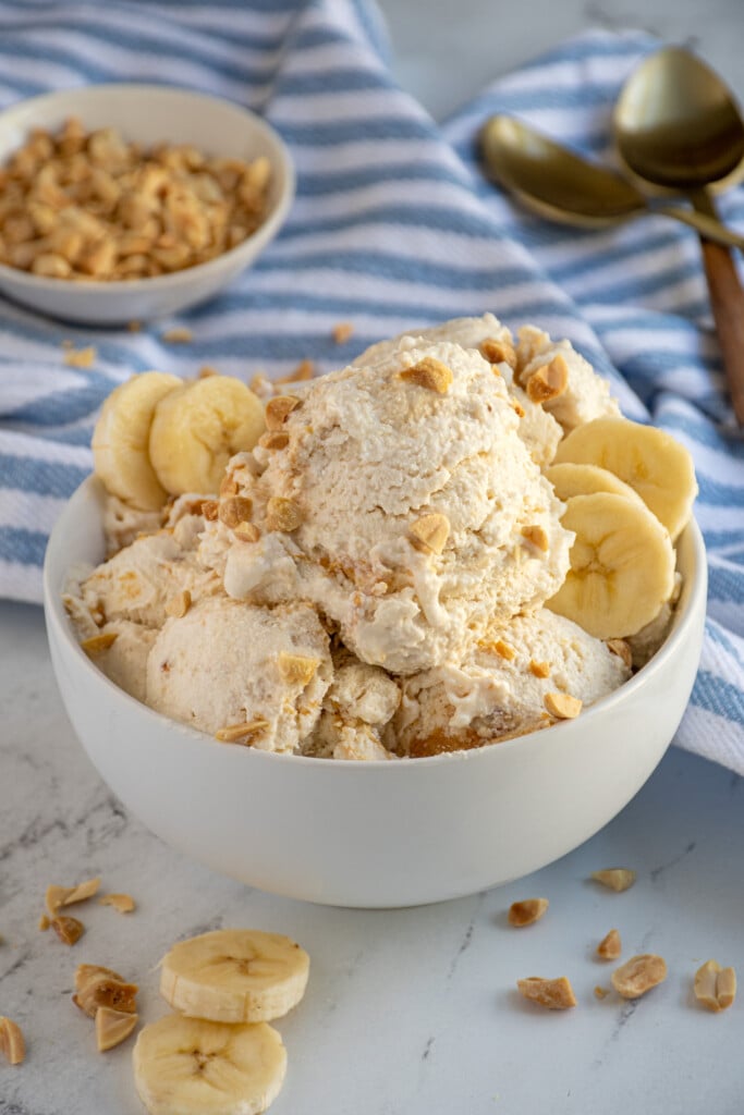 A bowl filled with cottage cheese ice cream garnished with crushed peanuts and banana slices.