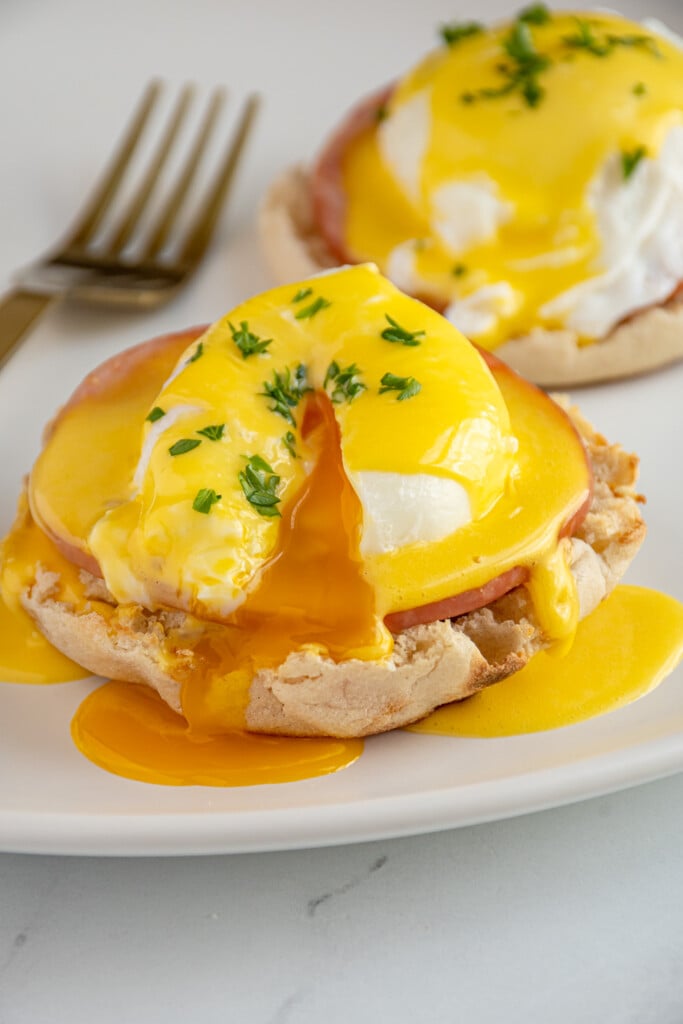 Easy eggs Benedict on a plate with the yolk of the poached egg broken open and dripping down the English muffin.