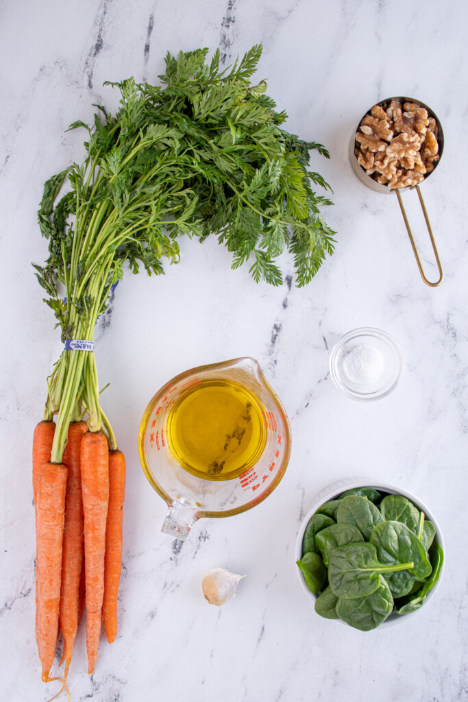 The ingredients needed to make carrot top pesto laid out on a tabletop.