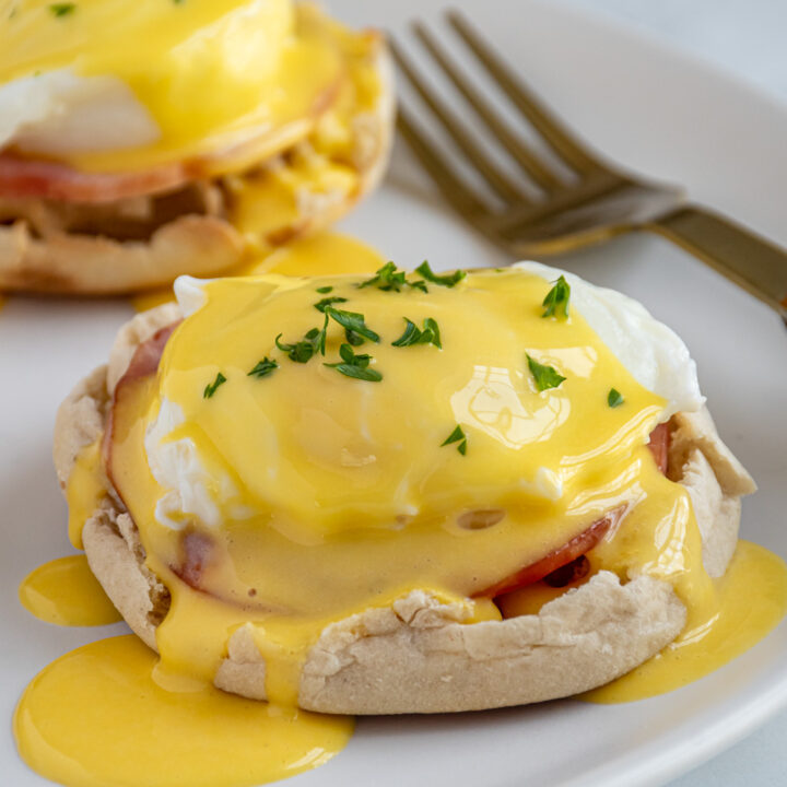 A white plate with eggs Benedict with hollandaise sauce.