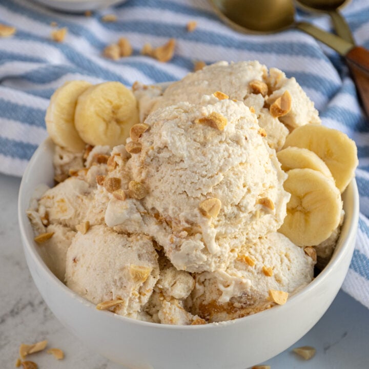 A bowl filled with scoops of cottage cheese ice cream with peanuts and banana slices as garnish.