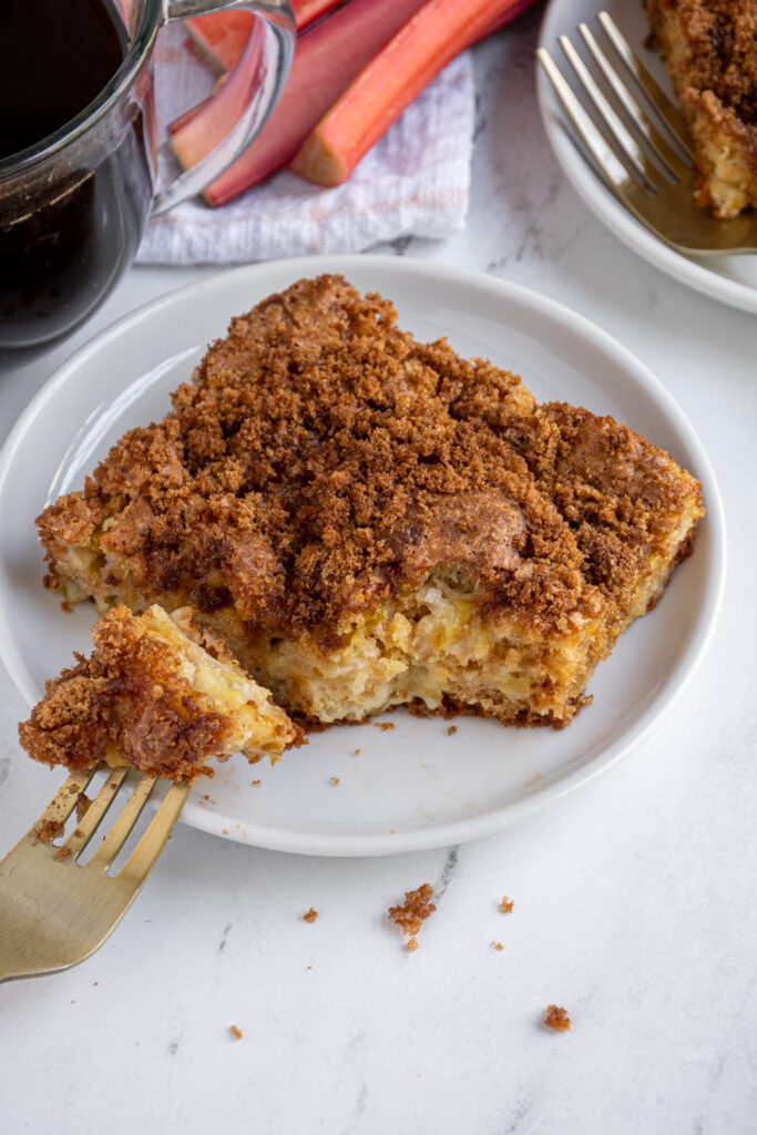A slice of rhubarb coffee cake on a plate with a bite of it on a fork.