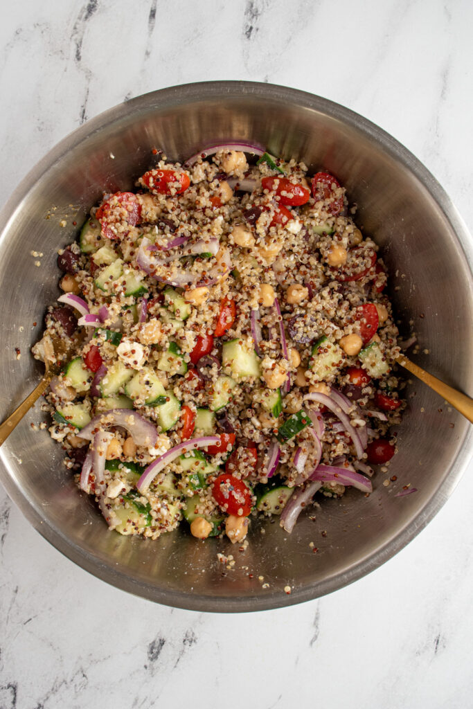 A stainless steel bowl filled with greek quinoa salad with chickpeas.