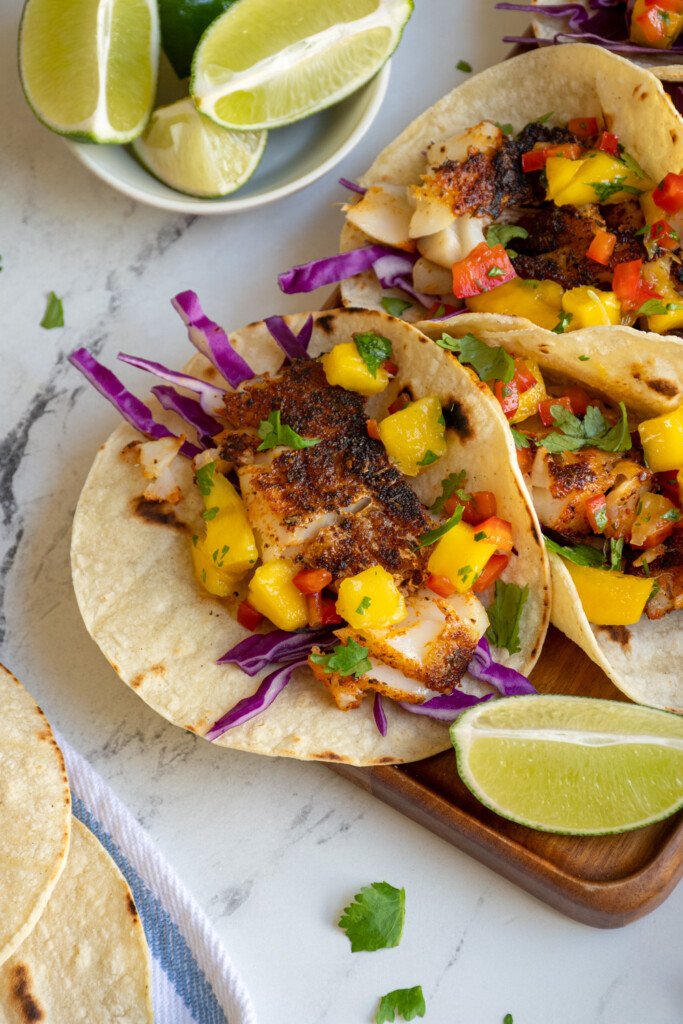 A platter with a close up of a tortilla filled with cabbage, blackened fish, and mango salsa.