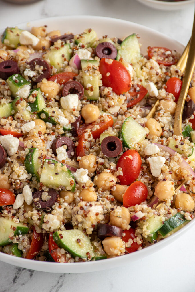 Close up of greek quinoa chickpea salad in a white bowl.