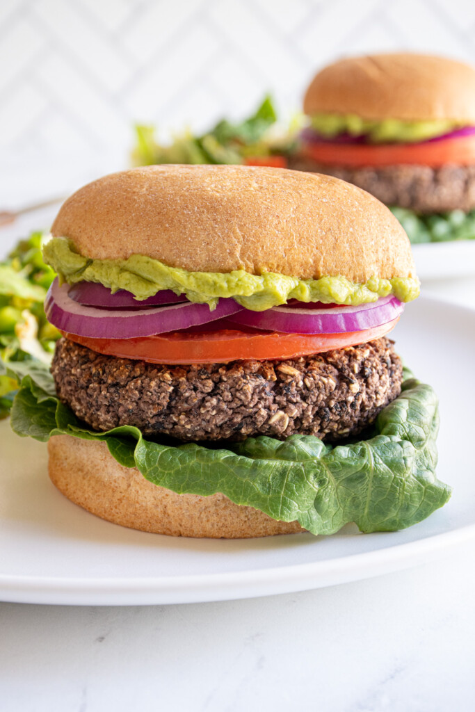 A black bean burger in a bun with lettuce, tomato, onion, and guacamole.