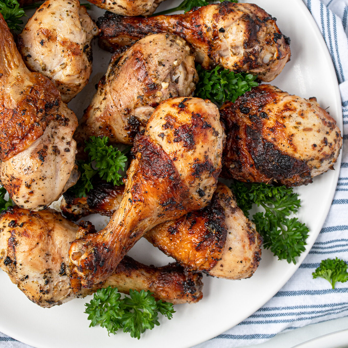 A white plate full of grilled greek marinated chicken drumsticks showing off crispy brown skins.