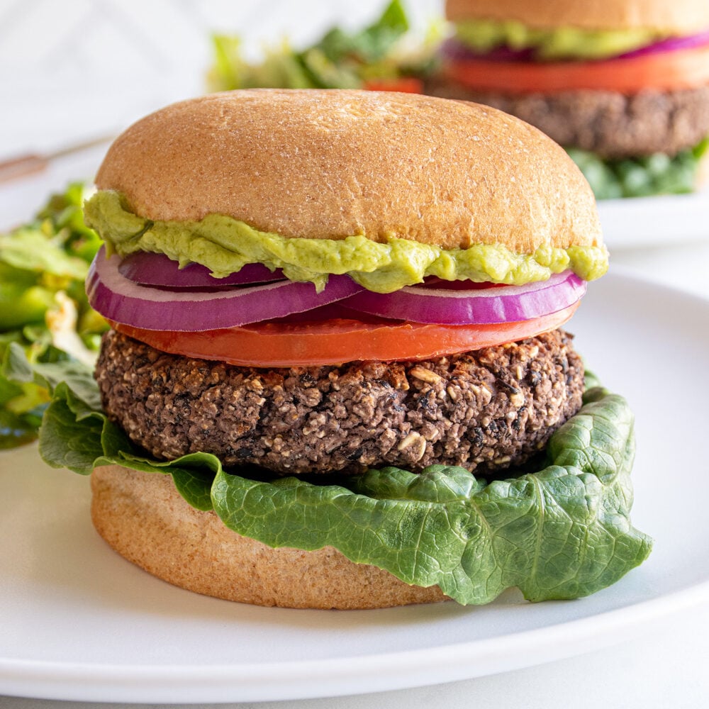 A grilled black bean burger on a bun with lettuce, tomato, red onion, and guacamole.