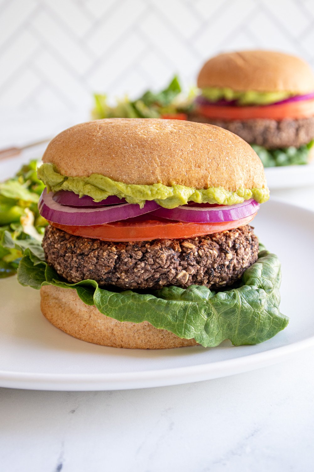 A grilled black bean burger on a bun with lettuce, tomato, red onion, and guacamole.