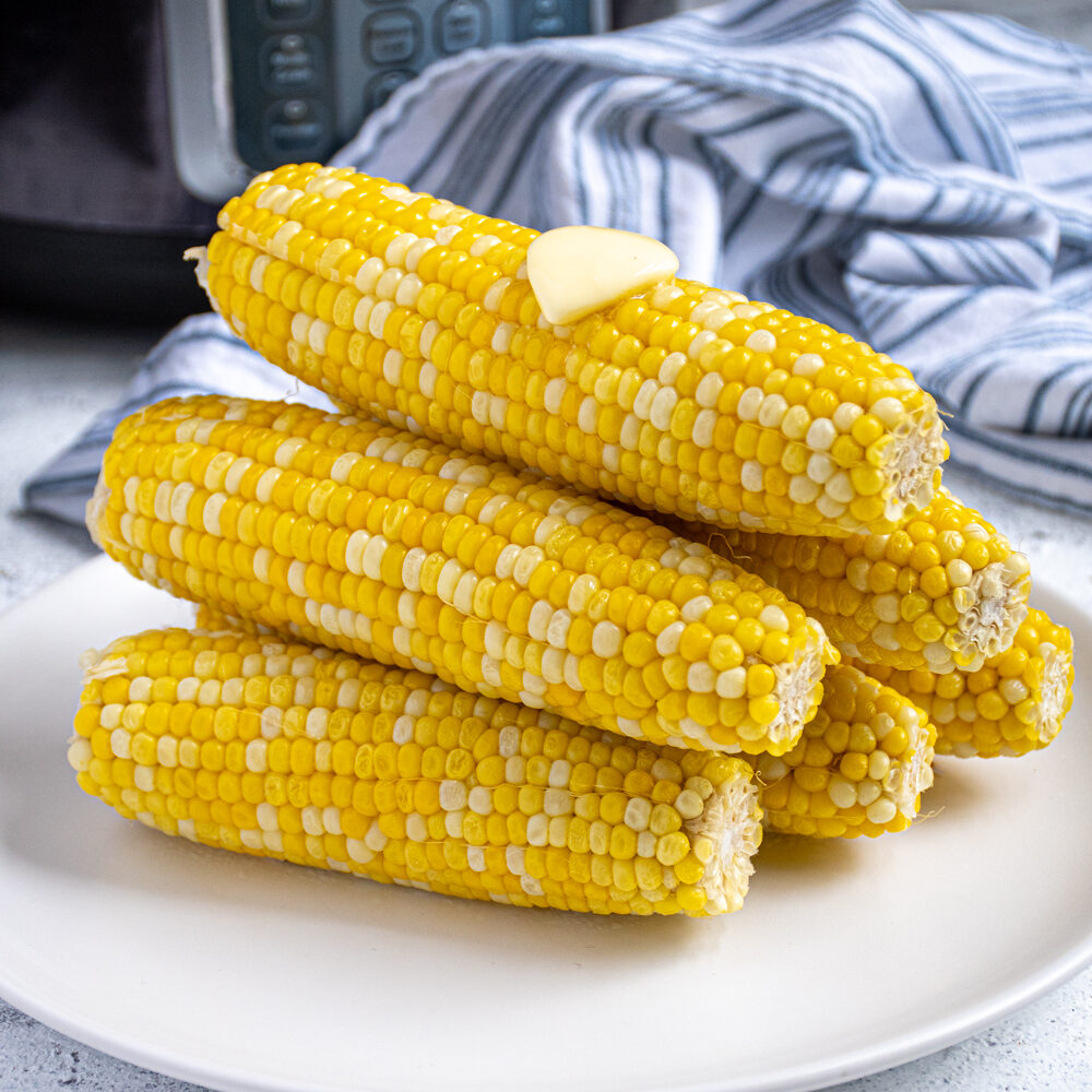 Pyramid shaped stack of freshly cooked instant pot corn on the cob showing off bright yellow kernels complete with a slab of melted butter on top.
