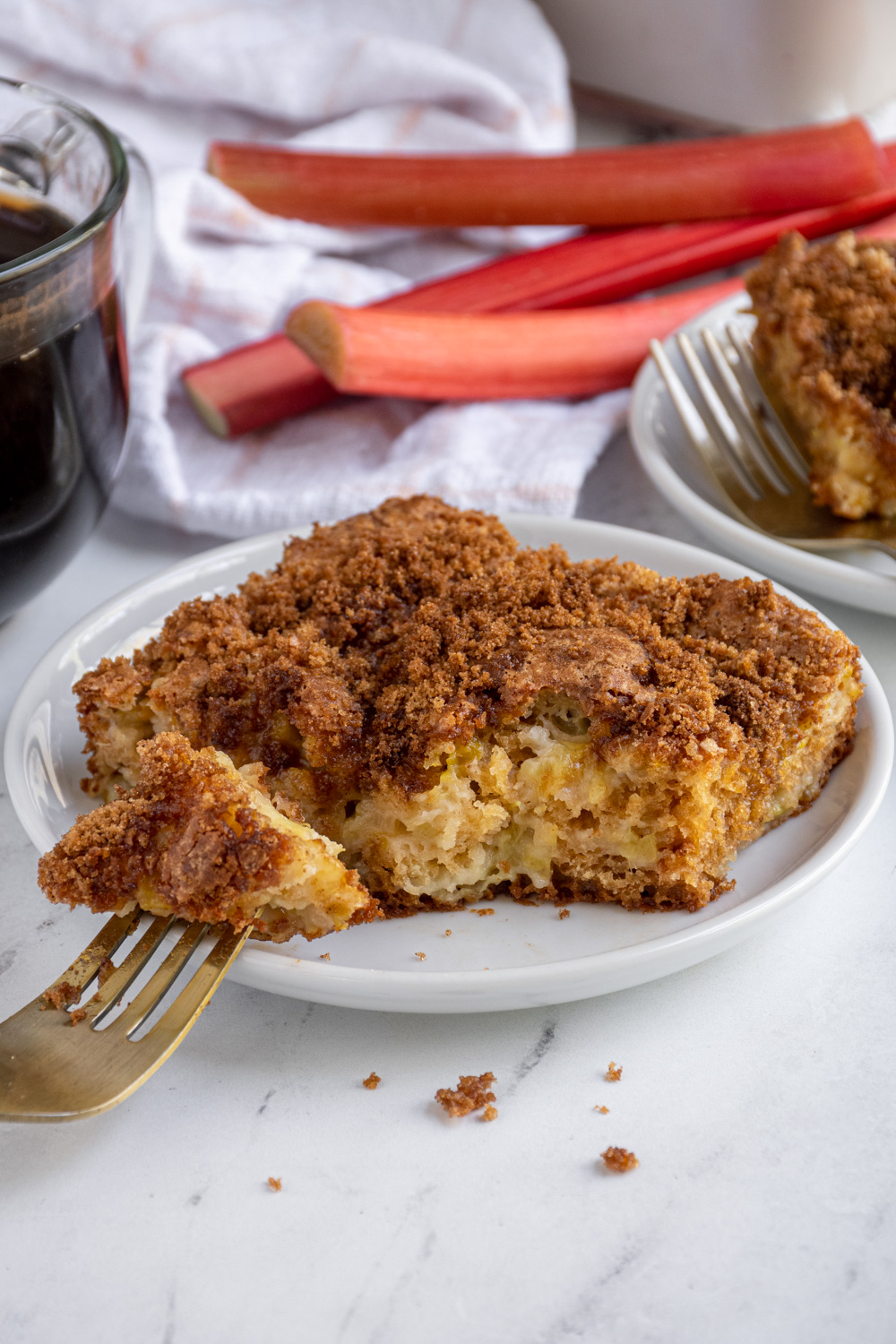 A plate with a slice of rhubarb coffee cake with a bite on a fork.